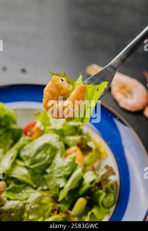 Gros plan d'une fourchette tenant une crevette et une laitue sur une assiette à salade fraîche et vibrante Banque D'Images