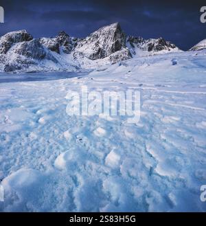 Spectaculaire paysage de nature arctique d'hiver de nuages de ciel de couleur de coucher de soleil, l'eau de mer côtière gelée et les sommets de montagnes enneigées. Norvège, Lofoten. Banque D'Images