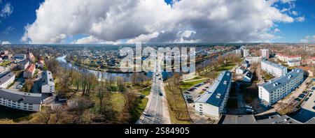 Vue aérienne panoramique d'une petite ville divisée par une rivière sinueuse, avec un pont, des espaces verts et une église avec une grande flèche sous un clou spectaculaire Banque D'Images