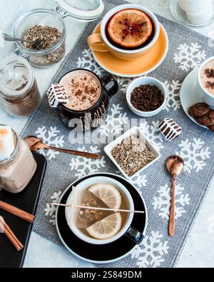 Une installation confortable avec des boissons chaudes, des épices, des guimauves et des bâtons de cannelle sur une nappe à motifs flocon de neige, avec des tons chauds et des détails festifs. Banque D'Images