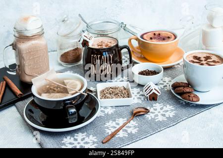 Arrangement confortable de boissons chaudes dans diverses tasses avec des maisons en pain d'épice, des biscuits, des bâtonnets de cannelle, et des pots de poudre de cacao et de guimauves. Banque D'Images