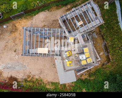 Vue aérienne d'un chantier de construction avec charpente en acier, panneaux isolants jaunes, équipement et sol sablonneux entouré d'herbe et de végétation Banque D'Images