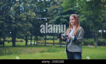 Femme d'affaires pilotant un drone à l'aide d'une télécommande dans un parc de la ville, profitant d'une nouvelle technologie Banque D'Images