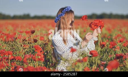 Femme slave portant des fleurs bleues couronne cueillant des coquelicots dans un beau champ de coquelicots au coucher du soleil Banque D'Images