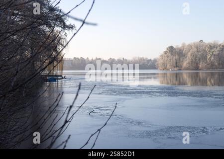 Une scène hivernale sereine à Straussee, avec une eau partiellement gelée reflétant les arbres couverts de gel sous un ciel bleu clair. Banque D'Images