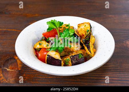 Plat de légumes fraîchement préparé avec des dés d'aubergines et de tomates, garni d'herbes, servi dans un bol blanc sur une table en bois. Un me séduisant Banque D'Images