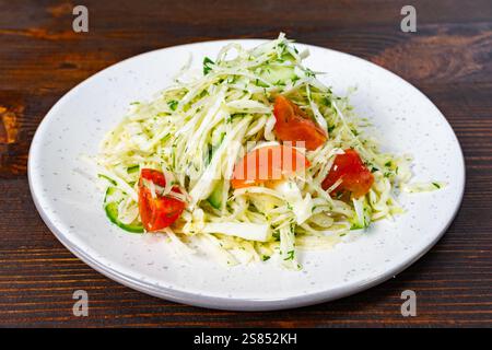 Une salade vibrante composée de chou râpé, de tomates mûres et d'herbes fraîches est élégamment disposée sur une assiette blanche. Ce plat est parfait pour une bonne santé Banque D'Images