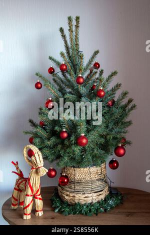 Un présentoir de Noël d'inspiration scandinave avec un arbre artificiel décoré en rouge dans un pot de paille, accompagné d'une chèvre Yule traditionnelle. Banque D'Images