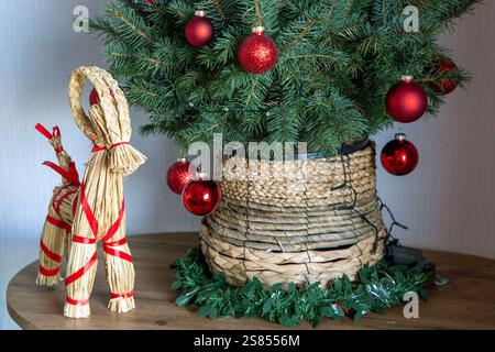 Un présentoir de Noël d'inspiration scandinave avec un arbre artificiel décoré en rouge dans un pot de paille, accompagné d'une chèvre Yule traditionnelle. Banque D'Images