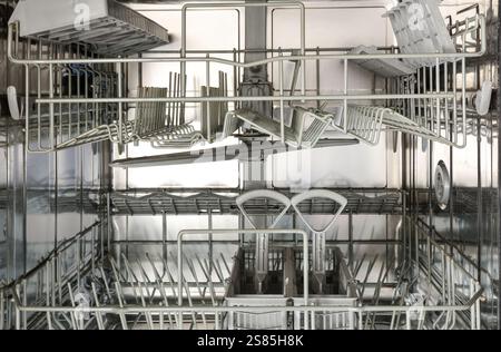Intérieur d'un lave-vaisselle vide et propre en acier inoxydable avec deux supports à ustensiles et panier en plastique. Vue de face. Banque D'Images