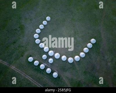 Ligne de yourtes blanches dans un motif courbe sur une plaine herbeuse, vue d'en haut près du lac Song Kol, Kirghizistan Banque D'Images