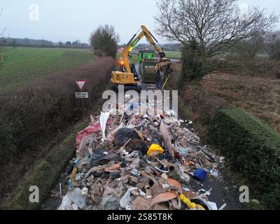 Les entrepreneurs travaillent à enlever le tas de déchets de 10 pieds de haut de Watery Lane, à la périphérie de Lichfield dans le Staffordshire. Les autorités locales recherchent des preuves vidéo pour retrouver les mouches qui ont déversé un énorme monticule de déchets de construction s'étendant sur plus de 40 pieds le long d'une route à deux voies, bloquant l'accès aux maisons et aux entreprises. Date de la photo : mardi 21 janvier 2025. Banque D'Images
