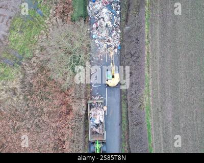 Les entrepreneurs travaillent à enlever le tas de déchets de 10 pieds de haut de Watery Lane, à la périphérie de Lichfield dans le Staffordshire. Les autorités locales recherchent des preuves vidéo pour retrouver les mouches qui ont déversé un énorme monticule de déchets de construction s'étendant sur plus de 40 pieds le long d'une route à deux voies, bloquant l'accès aux maisons et aux entreprises. Date de la photo : mardi 21 janvier 2025. Banque D'Images