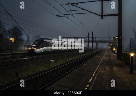 Un train moderne et élégant s'arrête à un quai de gare déserte sous un ciel nocturne mystérieux et brumeux. Banque D'Images