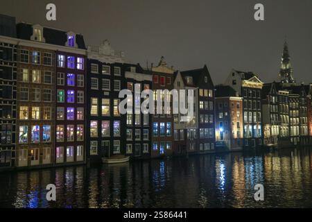 Vue en soirée des maisons dansantes : maisons hollandaises traditionnelles le long d'un canal à Amsterdam, aux pays-Bas, avec fenêtres éclairées et reflets dans l'eau Banque D'Images