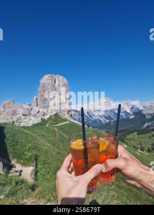 Mains tenant des boissons rafraîchissantes contre le ciel bleu clair dans les montagnes. Deux amis acclamant avec des verres de boissons rafraîchissantes aperol Spritz Banque D'Images