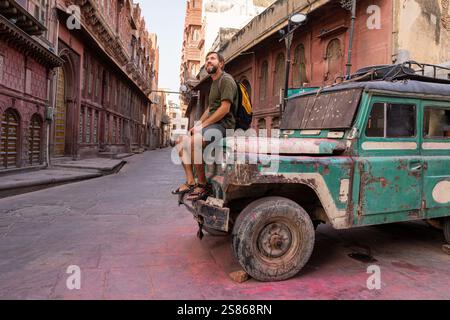 Touriste masculin assis sur le capot de vieux wack d'une voiture à Bikaner, Rajasthan, Inde Banque D'Images