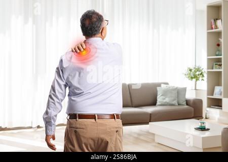 Vue arrière d'un homme âgé à domicile souffrant de douleurs de l'épaule Banque D'Images