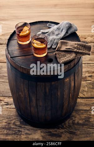 Deux verres de boisson d'hiver avec des tranches d'orange placées sur un tonneau rustique, jumelés avec des gants de laine, capturant l'essence de l'hiver chaud et créatif Banque D'Images