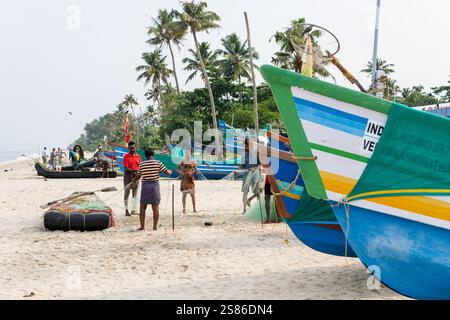 KERALA, INDE - 18 AVRIL 2024 : pêcheurs indiens c;se penchant des filets de pêche près des bateaux traditionnels en bois sur la plage de Marari. Banque D'Images