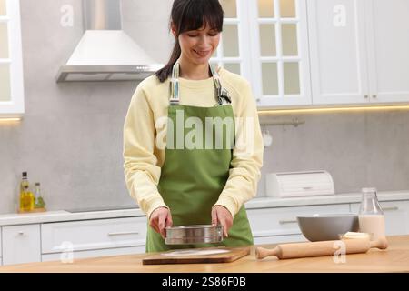 Femme saupoudrant la farine sur une planche de bois avant de rouler la pâte à table à l'intérieur Banque D'Images