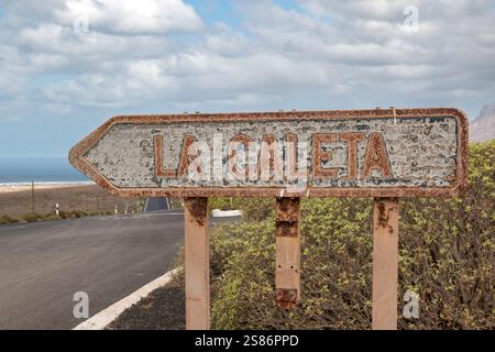 Panneau de direction pour un village la Caleta. Proche de l'océan Atlantique, rouillé à cause du vent salé. Lanzarote, Îles Canaries, Espagne. Banque D'Images