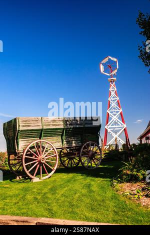 Un grand moulin à vent est à côté d'un wagon en bois. La scène est paisible et sereine, avec le moulin à vent et le wagon debout dans un champ herbeux Banque D'Images