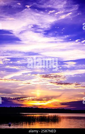 Le ciel est une belle nuance de violet et de bleu. Le soleil se couche, projetant une lueur chaude sur l'eau. Les nuages sont dispersés dans le ciel, Banque D'Images