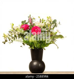 Vase noir avec des fleurs roses et blanches, et feuillage vu sur un fond blanc. Banque D'Images