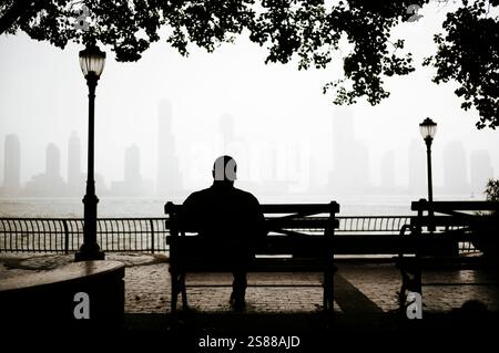 Silhuete d'un homme assis sur un banc avec vue de Manhattan ville en arrière-plan, New York, États-Unis Banque D'Images