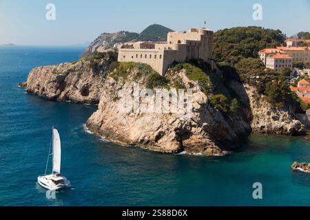Construit sur d'excellents affleurements rocheux défensifs avec des falaises abruptes, Fort Lovrijenac ou forteresse Saint-Laurent, forteresse italienne di San Lorenzo, souvent appelé 'Gibraltar de Dubrovnik', est une forteresse et un théâtre en dehors de la vieille ville fortifiée / vieille ville de Dubrovnik. Croatie. Un bateau yacht coûteux navigue autour de la côte devant le château. (138) Banque D'Images