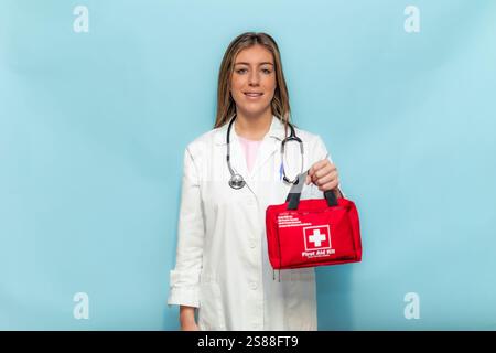 Jeune femme médecin confiante portant un manteau blanc et un stéthoscope tenant une trousse de premiers soins rouge, fournissant un sentiment de préparation et d'expertise médicale Banque D'Images