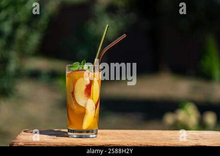 Un verre d'un cocktail d'été ou un thé froid avec des tranches de pêche, de la glace et de la menthe sur le fond de la nature. Gros plan Banque D'Images