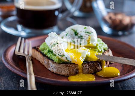 Couper l'oeuf poché avec le jaune d'oeuf liquide sur le pain grillé avec la purée d'avocat étalé dans l'assiette, gros plan. Petit-déjeuner ou déjeuner sain Banque D'Images