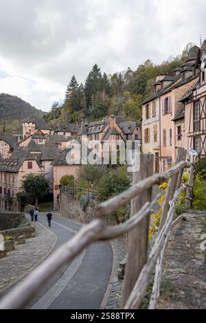 Rue idyllique dans le village médiéval de Conques, Aveyron, France, avec des maisons traditionnelles à colombages, des murs en pierre et une végétation luxuriante Banque D'Images