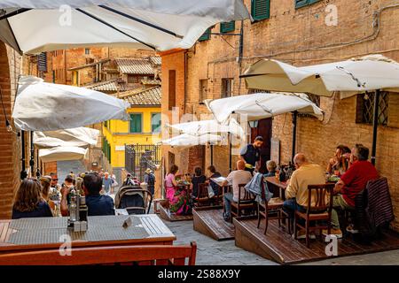 Les gens assis à manger dans deux restaurants qui sont côte à côte sur Costa Sant'Antonio une rue étroite très escarpée à Sienne, Italie Banque D'Images