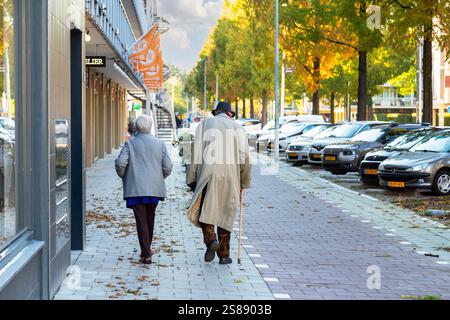 Deux personnes âgées marchent difficilement sur le trottoir d'une rue commerçante déserte dans une banlieue de la grande ville d'Amsterdam. Banque D'Images