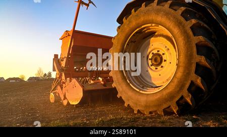 Agriculteur avec tracteur conduisant à travers une flaque dans le pré pendant la tonte. Des éclaboussures de saleté s'échappent des roues. Banque D'Images