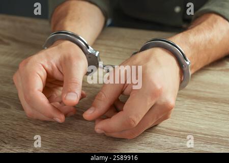 Homme menotté en métal à la table en bois, gros plan Banque D'Images