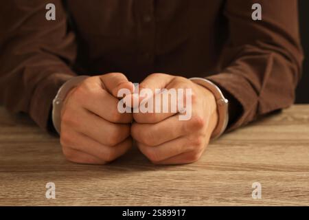 Homme menotté en métal à la table en bois, gros plan Banque D'Images