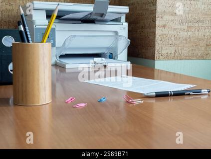 Une feuille de papier et un crayon couchés sur une table sur fond de fournitures de bureau. Une imprimante est en arrière-plan Banque D'Images