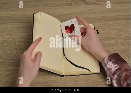 Les mains de la femme ont trouvé la carte de voeux de Saint-Valentin lettre romantique avec coeur rouge dans un cahier sur la table en bois Banque D'Images
