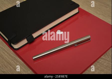 Carnet rouge avec coeur blanc, livre noir, stylo étalé sur table en bois. Préparation de la Saint-Valentin à la célébration Banque D'Images