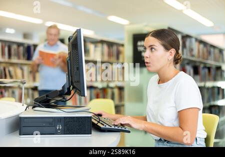 Une étudiante ciblée recherchant de l'information sur Internet sur un ordinateur fixe de la bibliothèque Banque D'Images