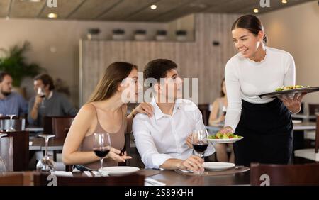 Serveuse amicale apportant des plats salade aux clients du restaurant Banque D'Images