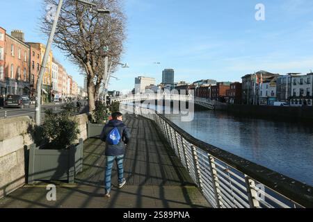 Dublin, Irlande - 17 janvier 2025 - d'un homme marchant le long de la promenade le long de la rivière Liffey vers le pont Ha'Penny dans le centre-ville de Dublin Banque D'Images