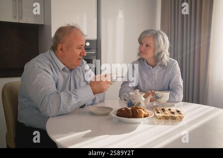 Couple senior apprécie l'heure du thé à la maison avec des collations et de la lumière naturelle Banque D'Images
