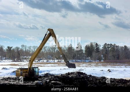 La pelle fonctionne sur un paysage enneigé, dégageant le terrain près des arbres lors d'une journée froide d'hiver sous la zone de fondation Banque D'Images