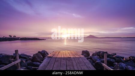 Vue sereine sur le coucher du soleil depuis le quai avec Manado Tua Island au loin et ciel coloré sur les eaux calmes Banque D'Images