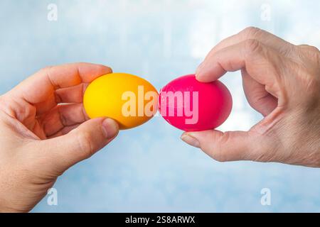 Tradition de Pâques de craquer des œufs, deux mains tiennent des œufs et essaient de casser l'œuf de l'autre, en gros plan sur fond bleu Banque D'Images
